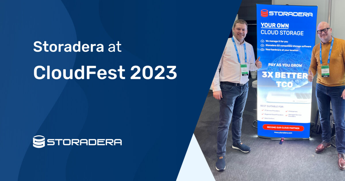 Tommi and Margus at CloudFest 2023 standing next to a Storadera banner looking happy.